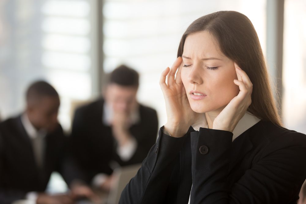 A woman rubbing her temples as two men sit in the background